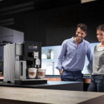 Paar im Gespraech neben der DeLonghi Maestosa auf einer dunklen Kuecheninsel